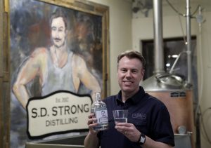 In this Jan. 19, 2018, photo, Steve Strong holds a bottle of gin at his S.D. Strong Distilling business in Parkville, Mo. Strong is planning to hire some part-time employees and buy some equipment as a result of the new tax law. (AP Photo/Charlie Riedel)