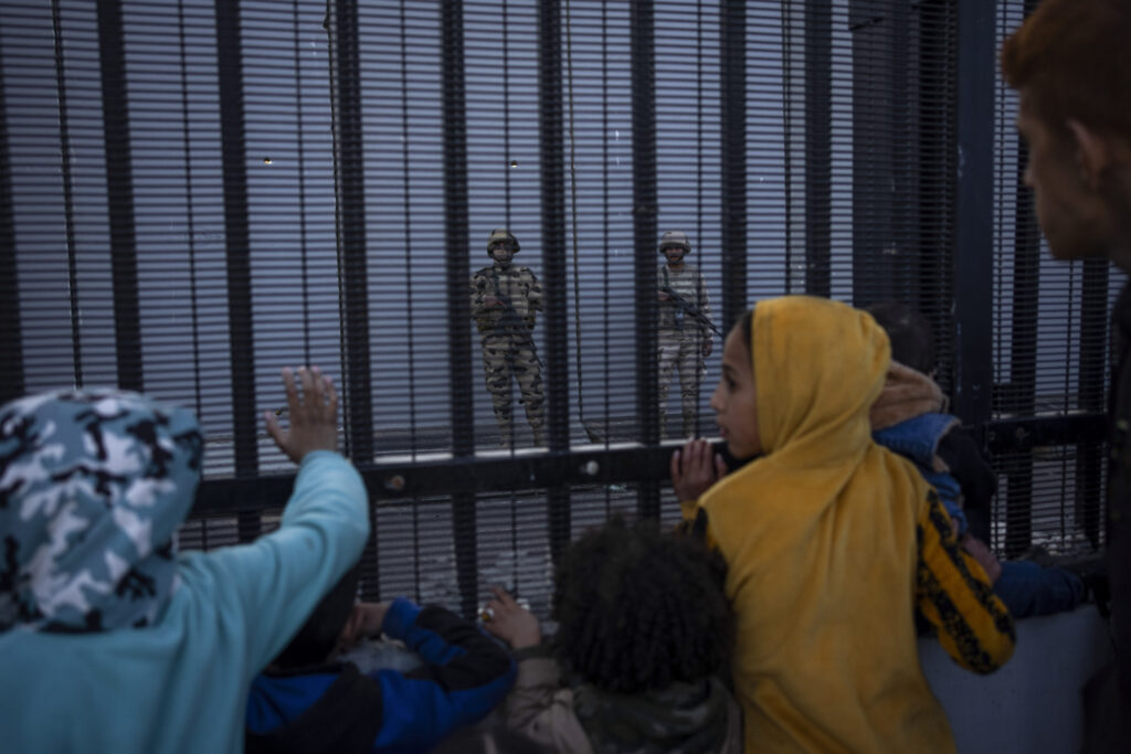 Displaced Palestinians look at Egyptian soldiers through the Egyptian border fence, in Rafah, southern Gaza, Sunday, Jan. 14, 2024.